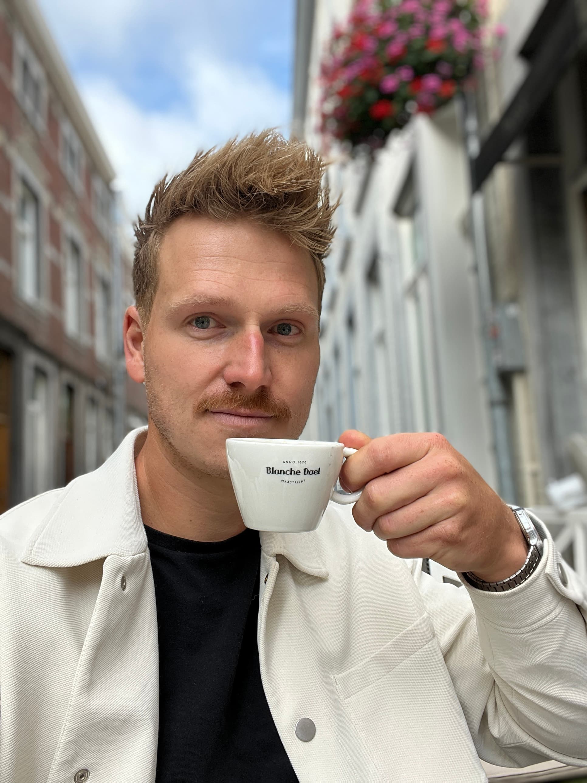 Nick Peters met een espressokopje op een terras in een Maastrichtse straat, kijkend in de camera.